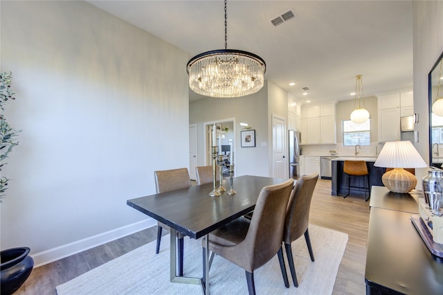 dining area with sink, an inviting chandelier, and light hardwood / wood-style flooring