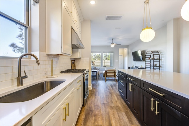 kitchen featuring gas range, sink, hanging light fixtures, and white cabinets