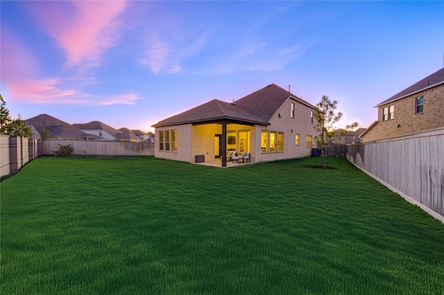 back house at dusk featuring a patio area and a lawn