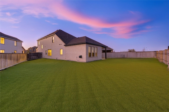 back house at dusk featuring a lawn