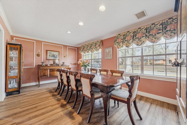 dining space with ornamental molding and light hardwood / wood-style floors