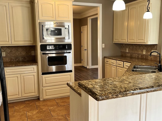 kitchen with sink, dark stone countertops, appliances with stainless steel finishes, kitchen peninsula, and pendant lighting