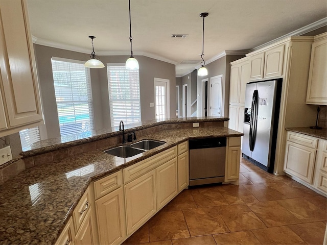 kitchen featuring appliances with stainless steel finishes, sink, dark stone countertops, hanging light fixtures, and cream cabinetry