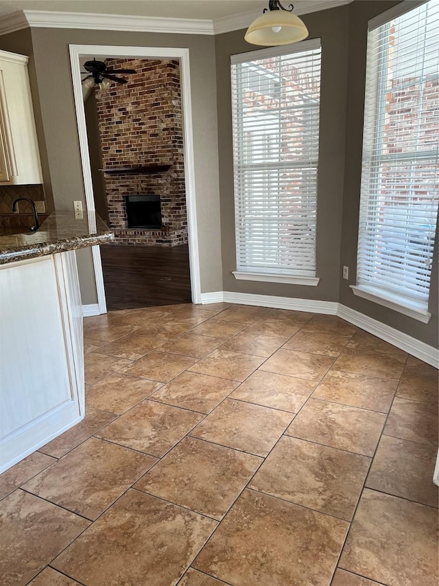 unfurnished dining area featuring crown molding, ceiling fan, light tile patterned flooring, and a brick fireplace