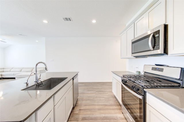 kitchen with sink, appliances with stainless steel finishes, light stone counters, light hardwood / wood-style floors, and white cabinets