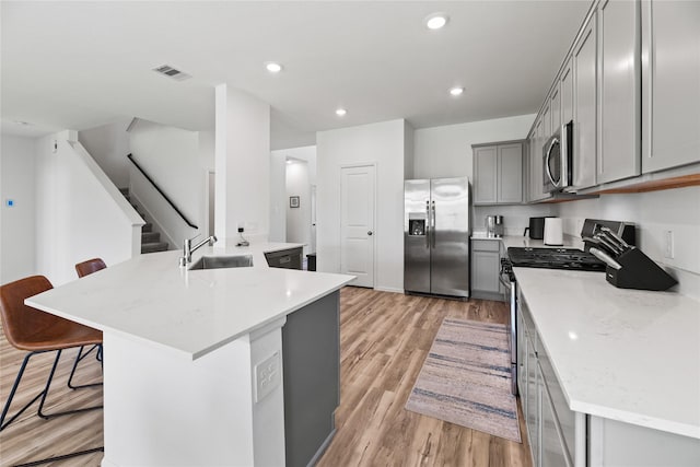 kitchen featuring a breakfast bar, sink, gray cabinetry, appliances with stainless steel finishes, and a kitchen island with sink