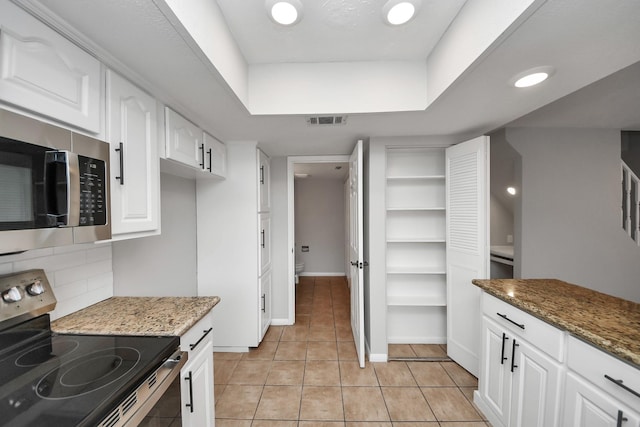 kitchen featuring light tile patterned flooring, white cabinetry, dark stone countertops, appliances with stainless steel finishes, and decorative backsplash