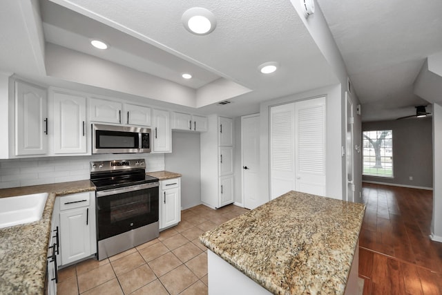 kitchen featuring light stone counters, appliances with stainless steel finishes, a raised ceiling, decorative backsplash, and white cabinets