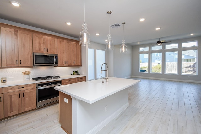 kitchen with appliances with stainless steel finishes, tasteful backsplash, an island with sink, sink, and hanging light fixtures