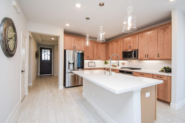 kitchen featuring decorative light fixtures, appliances with stainless steel finishes, an island with sink, light hardwood / wood-style floors, and backsplash