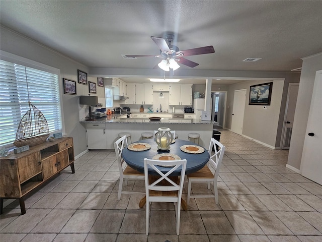 kitchen with white cabinetry, light tile patterned floors, kitchen peninsula, ceiling fan, and light stone countertops