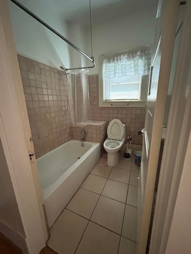 bathroom with toilet, tiled shower / bath combo, tile patterned flooring, and tile walls