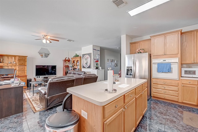 kitchen with ceiling fan, light brown cabinetry, a center island, and white oven