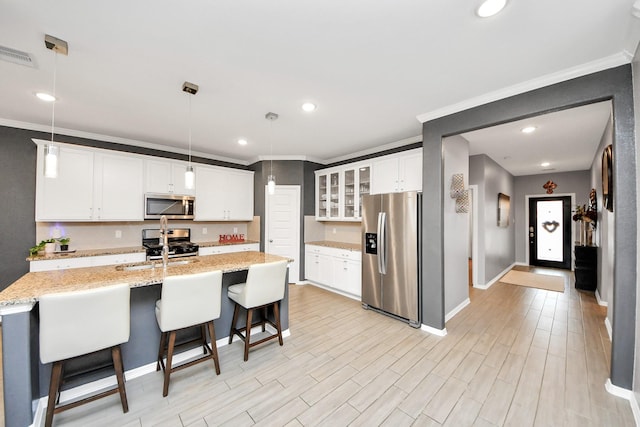 kitchen featuring white cabinetry, light stone counters, decorative light fixtures, a center island with sink, and stainless steel appliances