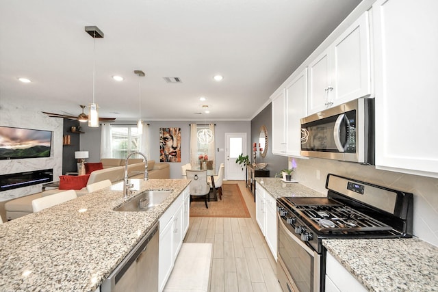 kitchen featuring pendant lighting, white cabinetry, sink, stainless steel appliances, and a premium fireplace