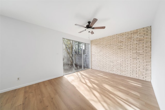 empty room with light hardwood / wood-style floors, ceiling fan, and brick wall