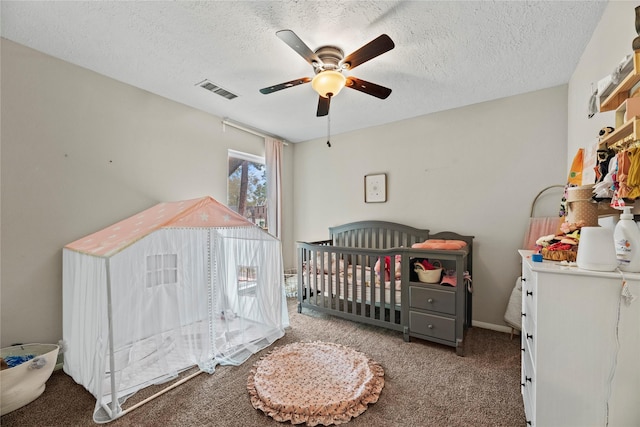 carpeted bedroom with ceiling fan, a nursery area, and a textured ceiling