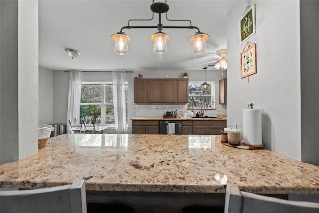 kitchen featuring sink, dishwasher, backsplash, hanging light fixtures, and kitchen peninsula