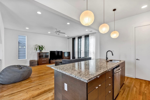 kitchen featuring pendant lighting, an island with sink, sink, light hardwood / wood-style floors, and light stone countertops