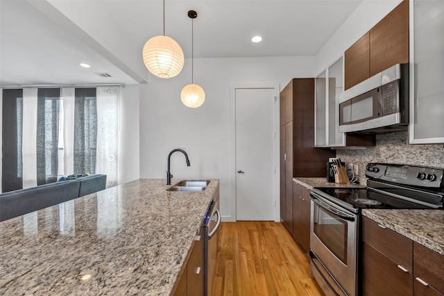 kitchen with pendant lighting, sink, light hardwood / wood-style flooring, appliances with stainless steel finishes, and light stone countertops