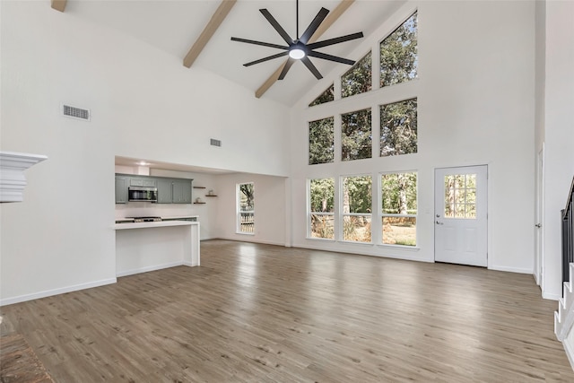 unfurnished living room featuring beamed ceiling, a wealth of natural light, hardwood / wood-style floors, and ceiling fan