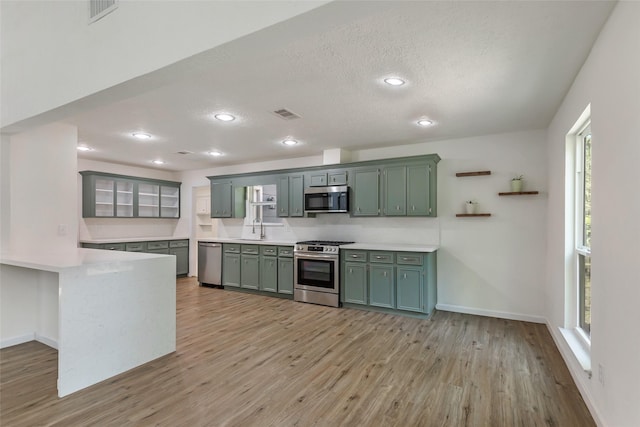 kitchen featuring sink, green cabinets, appliances with stainless steel finishes, light hardwood / wood-style floors, and a textured ceiling