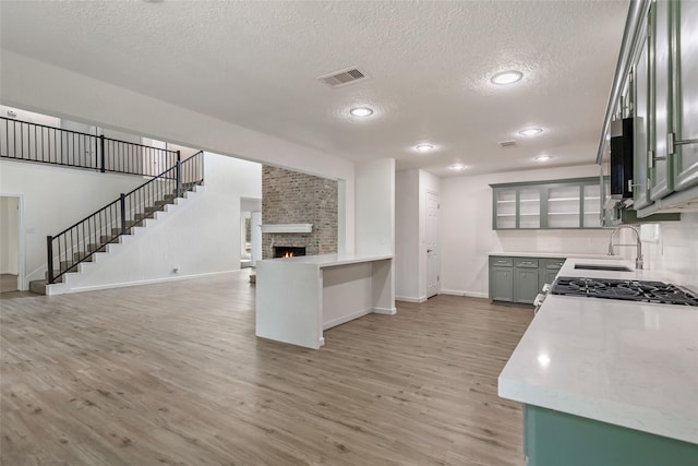 kitchen featuring sink, gray cabinetry, a fireplace, a textured ceiling, and light wood-type flooring