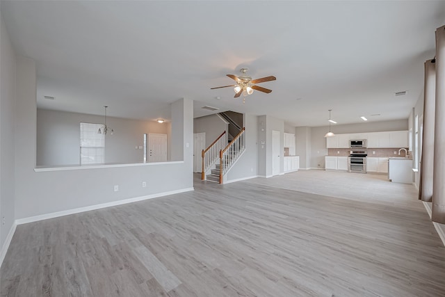 unfurnished living room featuring sink, ceiling fan with notable chandelier, and light hardwood / wood-style floors