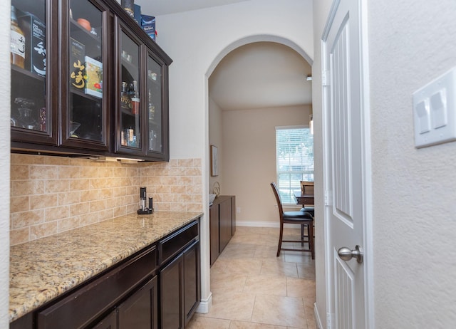 bar featuring tasteful backsplash, dark brown cabinetry, light stone countertops, and light tile patterned floors