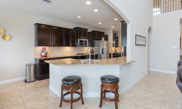 kitchen featuring sink, a breakfast bar, appliances with stainless steel finishes, light stone countertops, and decorative backsplash