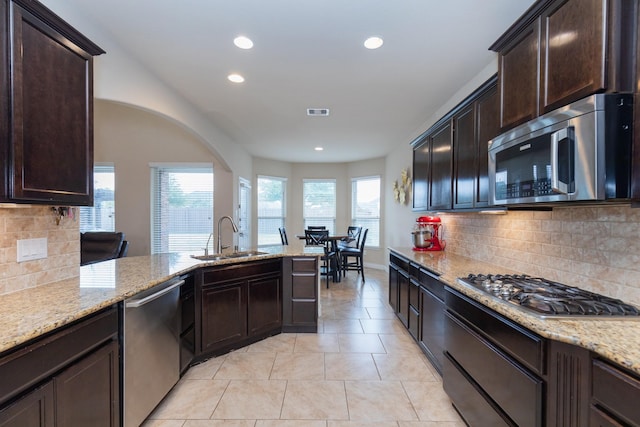 kitchen with stainless steel appliances, sink, dark brown cabinetry, and light stone counters