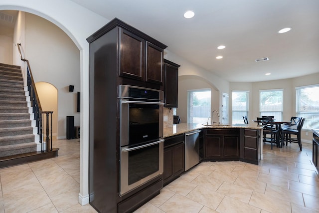 kitchen with appliances with stainless steel finishes, dark brown cabinets, a wealth of natural light, and light stone counters