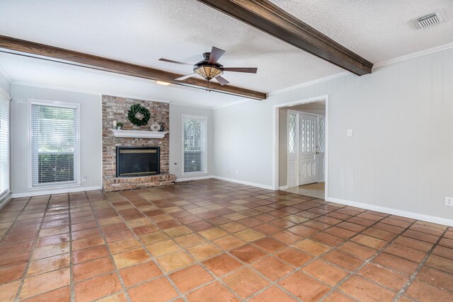 unfurnished living room with a brick fireplace, a textured ceiling, ornamental molding, ceiling fan, and beam ceiling