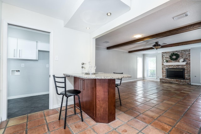 kitchen featuring a fireplace, a kitchen breakfast bar, dark tile patterned floors, ceiling fan, and beam ceiling