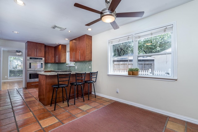 kitchen with backsplash, a kitchen breakfast bar, dark tile patterned floors, kitchen peninsula, and stainless steel double oven