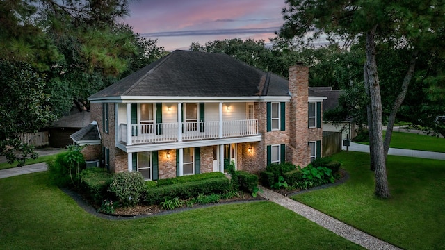 view of front facade with a balcony, a porch, and a yard