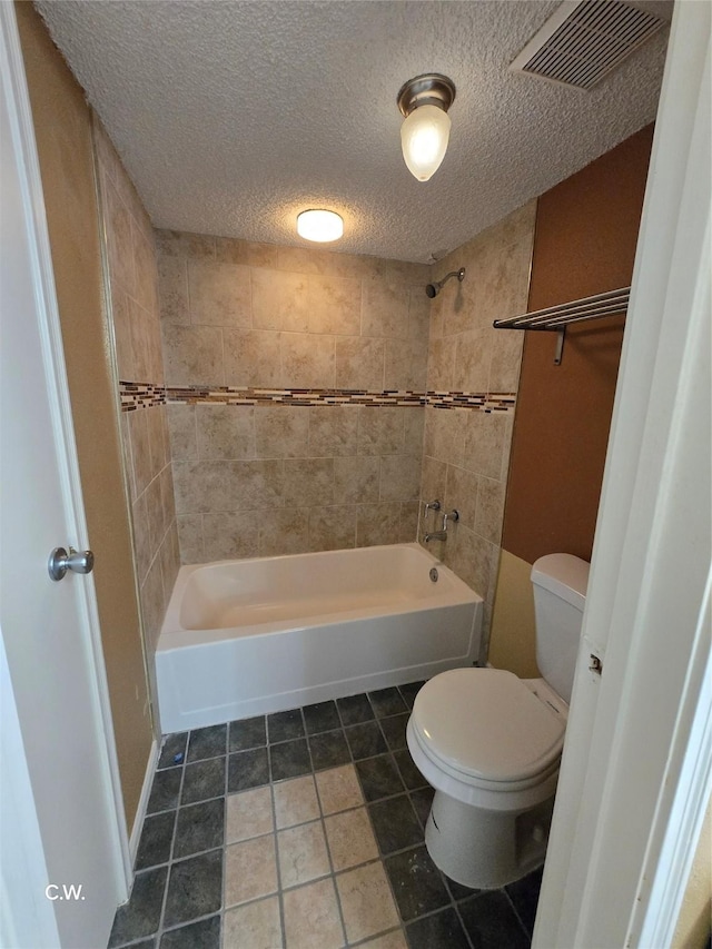 bathroom with tiled shower / bath, toilet, tile patterned flooring, and a textured ceiling