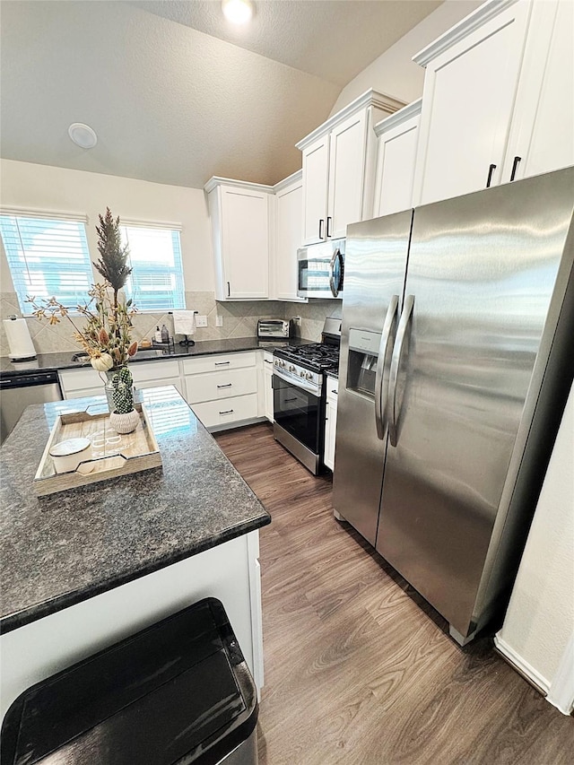 kitchen with white cabinetry, appliances with stainless steel finishes, dark hardwood / wood-style flooring, and dark stone countertops