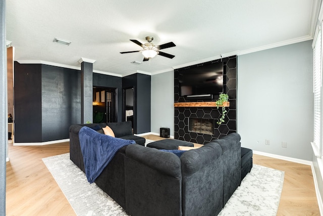 living room featuring hardwood / wood-style flooring, ceiling fan, ornamental molding, and a fireplace