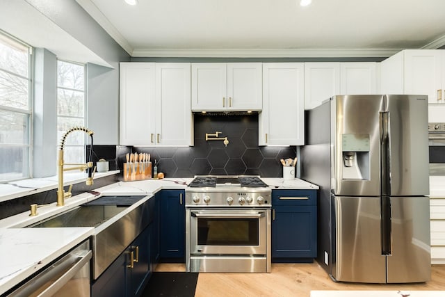 kitchen with appliances with stainless steel finishes, white cabinetry, decorative backsplash, light stone countertops, and blue cabinetry