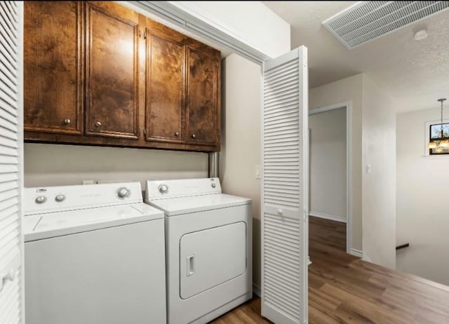 clothes washing area with washer and dryer, light hardwood / wood-style flooring, and cabinets