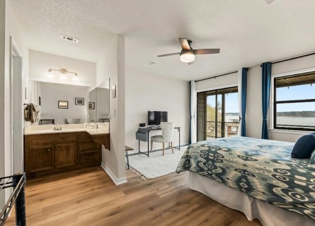 bedroom with sink, ensuite bath, a textured ceiling, access to outside, and light wood-type flooring