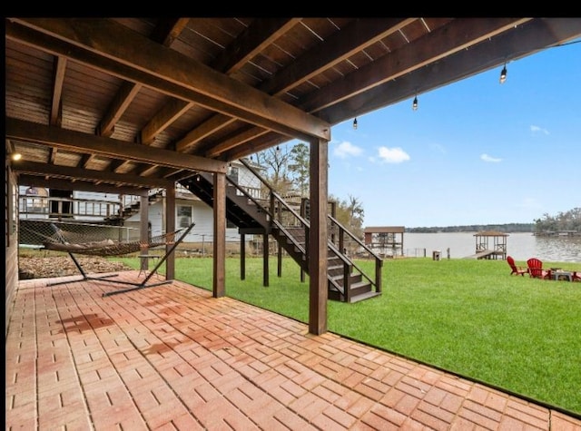 wooden terrace with a water view, a patio, and a lawn