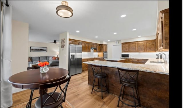 kitchen with appliances with stainless steel finishes, sink, kitchen peninsula, light stone countertops, and light hardwood / wood-style flooring