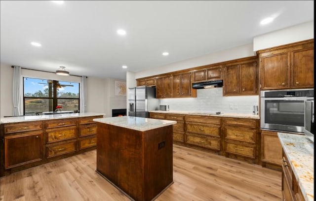 kitchen featuring light stone counters, a center island, light wood-type flooring, appliances with stainless steel finishes, and decorative backsplash