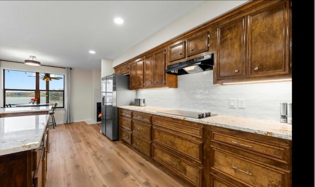 kitchen featuring stainless steel fridge, light stone counters, tasteful backsplash, black electric cooktop, and light wood-type flooring