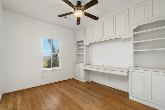 unfurnished office with ceiling fan, built in desk, and light hardwood / wood-style flooring