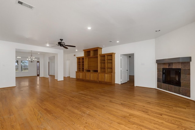 unfurnished living room with a tiled fireplace, ceiling fan with notable chandelier, and light wood-type flooring