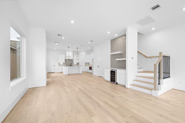 unfurnished living room with beverage cooler and light hardwood / wood-style flooring