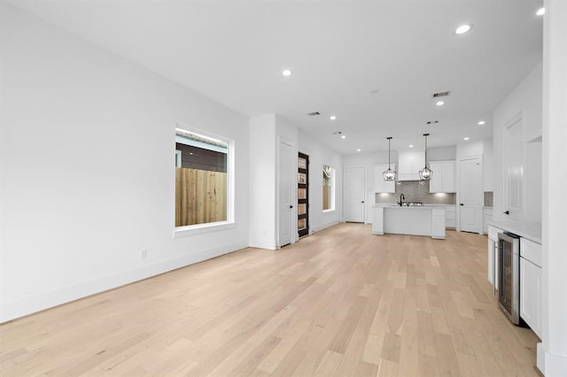 unfurnished living room featuring wine cooler, sink, and light hardwood / wood-style floors